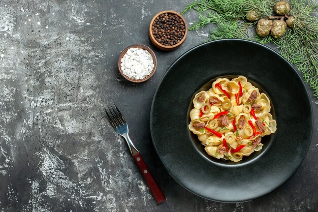 Delicious conchiglie with vegetables and greens on a plate and knife and different spices on gray background