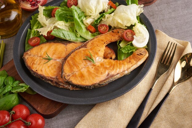 Delicious cooked salmon fish fillets. Grilled salmon fish fillet and fresh green lettuce vegetable tomato salad. Balanced nutrition concept for clean eating flexitarian mediterranean diet.