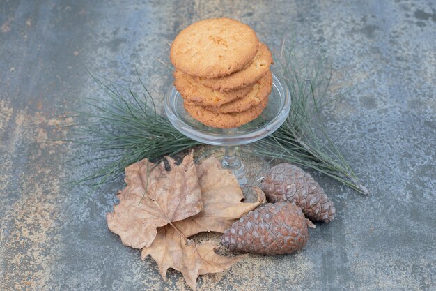 Delicious cookies in glass jar with leaves and pinecones on marble background. High quality photo