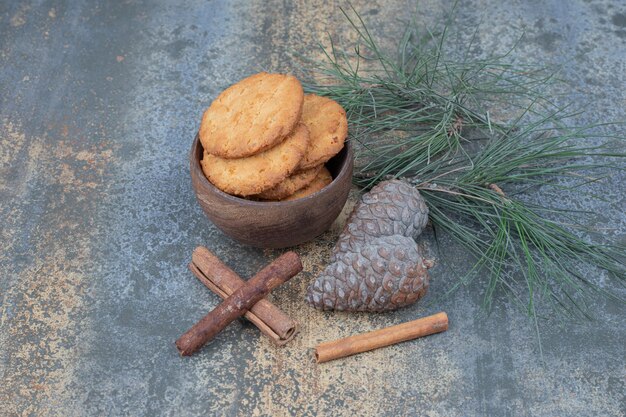 大理石のテーブルにシナモンスティックと松ぼっくりが付いた木製のボウルにおいしいクッキー。