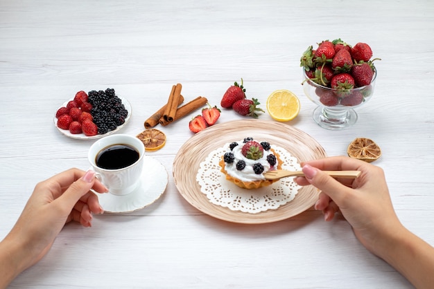 Free photo delicious creamy cake with berries getting eat by female with cinnamon coffee on light-white desk, cake photo color