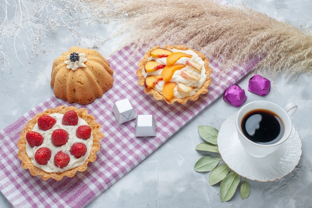 delicious creamy cakes with sliced fruits along with chocolate candies and tea on light desk, cake biscuit sweet cream bake tea sugar