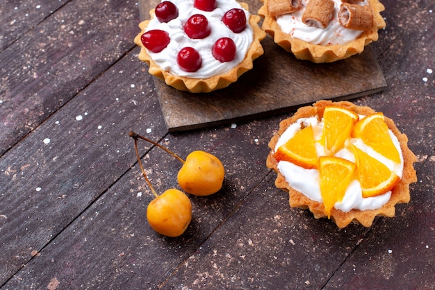 Free photo delicious creamy cakes with sliced fruits on brown wooden brown, cake biscuit fruit sweet bake