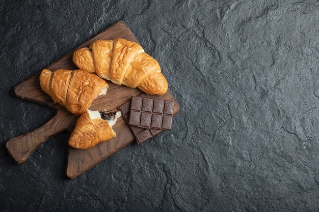 Delicious croissants with tasty chocolate bars on a wooden board. 