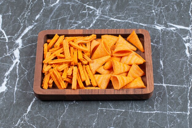 Delicious crunchy stick and triangle chips on wooden plate.