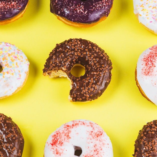 Delicious doughnuts with icing and missing bite on yellow background