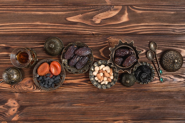 Delicious dried dates; nuts and tea on turkish vintage metallic bowl on wooden textured backdrop