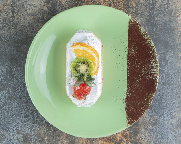 A delicious eclair with fruits on a green plate