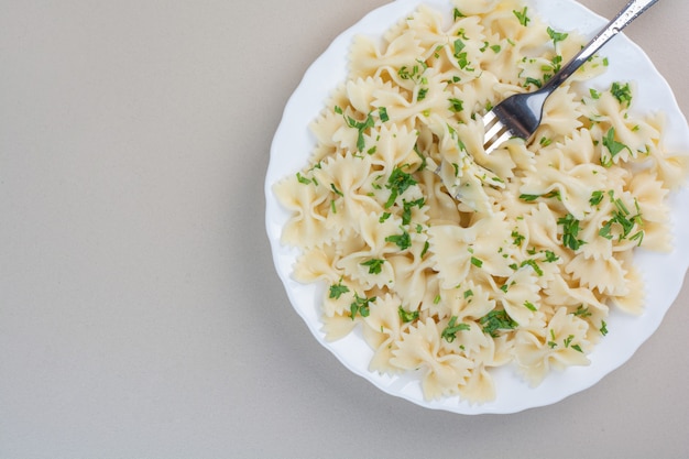 Delicious farfalle pasta with parsley and fork on white plate