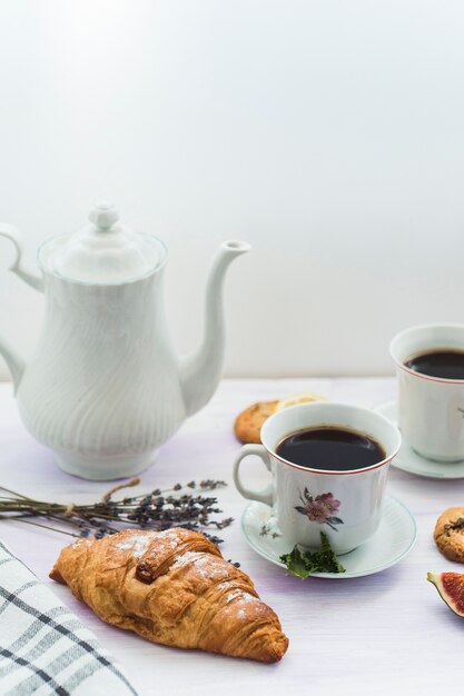Delicious fresh croissant with teapot and coffee on table