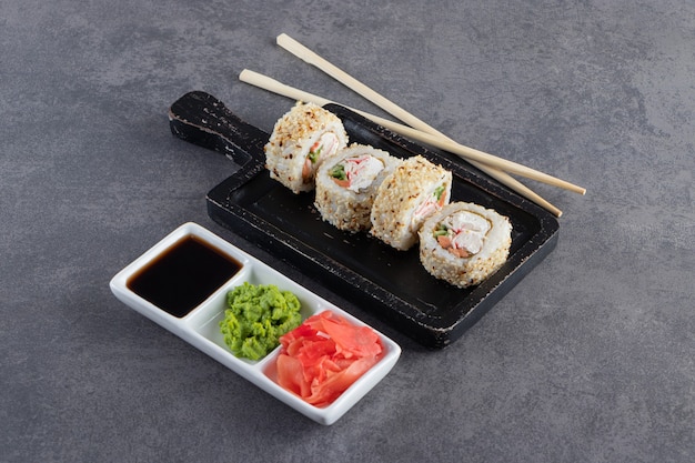 Delicious fresh sushi rolls with sesame seeds on black cutting board. 