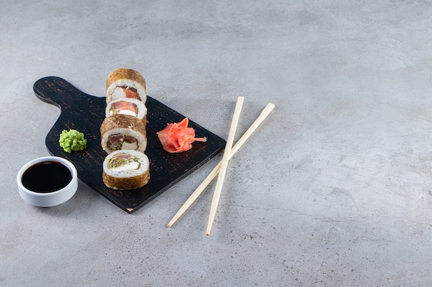 Вкусные свежие суши-роллы с соевым соусом и деревянными палочками на деревянной доске.