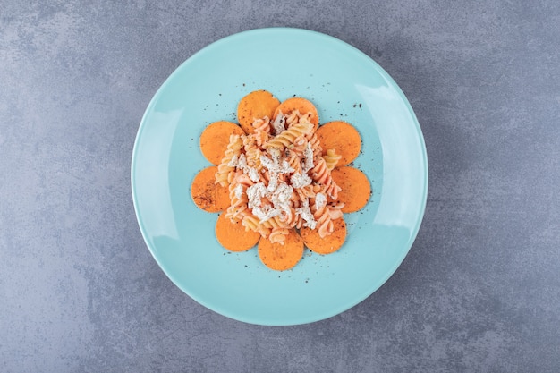 Delicious fusilli pasta and carrot on blue plate.