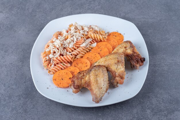 Delicious fusilli pasta and chicken wings on white plate.