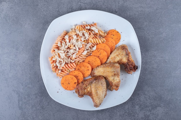 Delicious fusilli pasta and chicken wings on white plate.