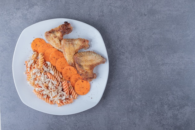 Delicious fusilli pasta and chicken wings on white plate.