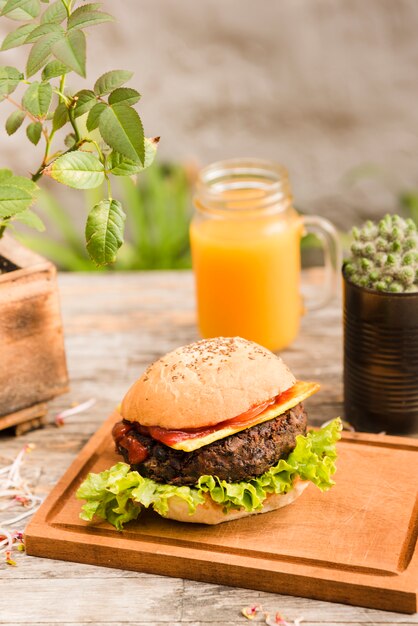 Вкусный гамбургер на разделочную доску с банкой сока на деревянный стол