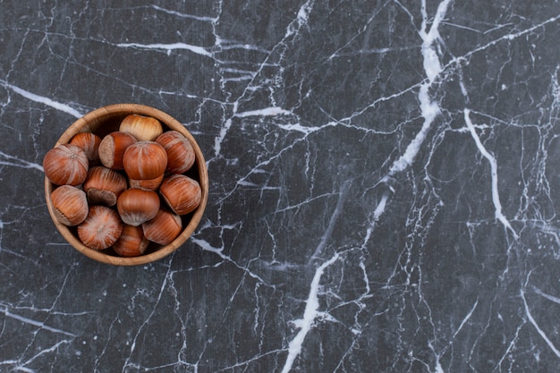 Delicious hazelnuts in wooden bowl over black stone.