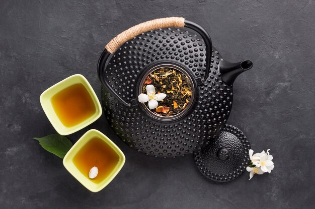 Delicious healthy herbal tea in bowl with black teapot on textured background