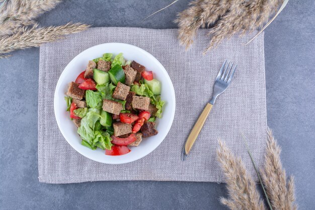 Delicious and healthy platter of shepherd's salad garnished with dried crust on a folded tablecloth with a fork on marble surface