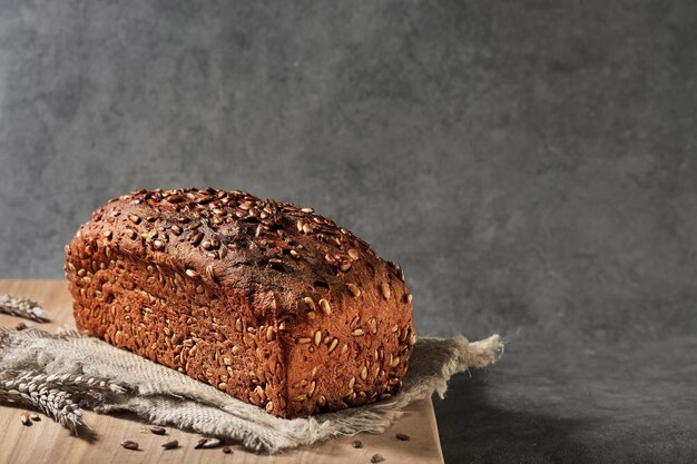 Delicious and healthy wheat - rye bread with seeds on sacking, close-up with selective focus. Fermented wholesome bread, healthy food. Loaf on gray background with space for text