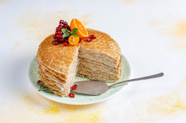 석류 씨와 만다린으로 장식 된 맛있는 수제 크레이프 케이크.