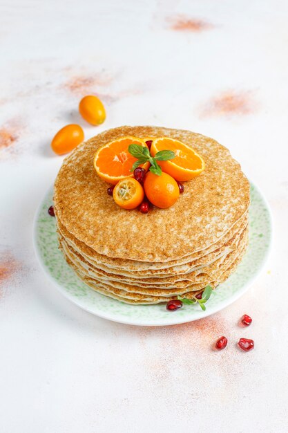 Delicious homemade crepe cake decorated with pomegranate seeds and mandarins.
