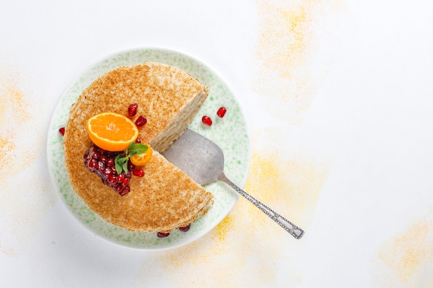 Delicious homemade crepe cake decorated with pomegranate seeds and mandarins.