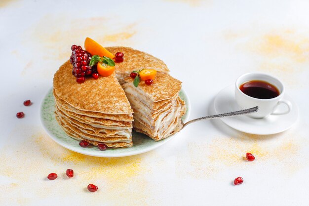 Delicious homemade crepe cake decorated with pomegranate seeds and mandarins.