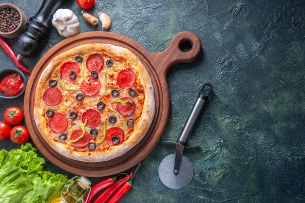 Delicious homemade pizza on wooden cutting board tomatoes garlic ketchup green bundle oil bottle pepper on dark surface in close up shot