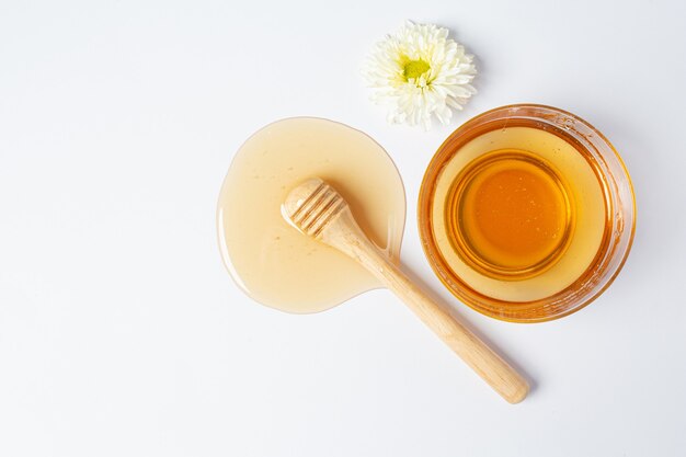 Delicious honey with wooden honey dipper on white surface