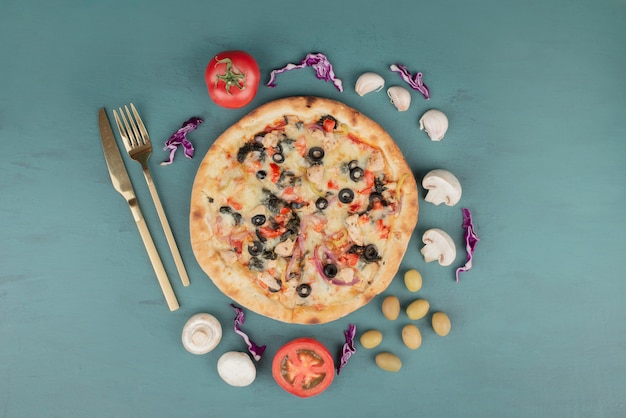 Free photo delicious hot pizza with olives, mushrooms and tomatoes on blue surface.