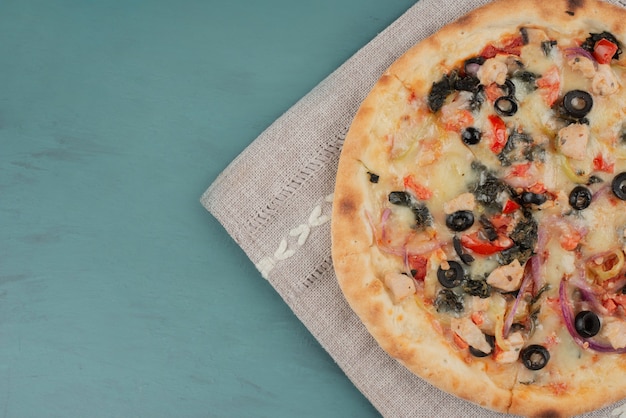 Deliziosa pizza calda con olive e pomodori sul tavolo blu.