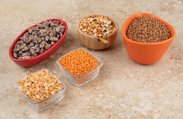 Delicious lentils and beans in plates on marble surface 