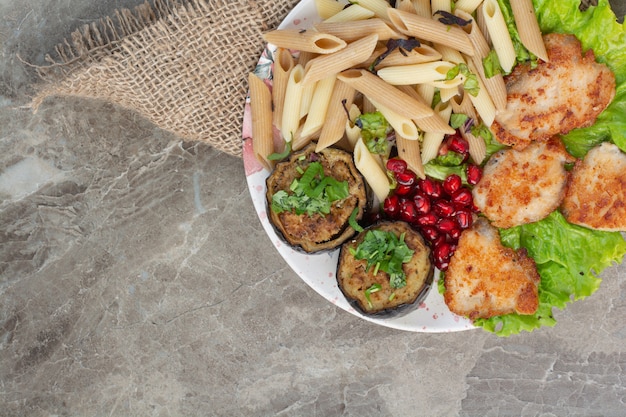 Delicious macaroni with pomegranate and lettuce on white plate.