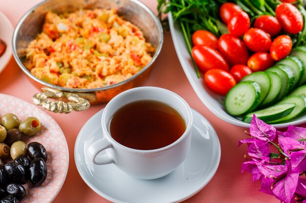 Delicious meal in a pot with a cup of tea, olive, salad, flowers high angle view on a pink surface