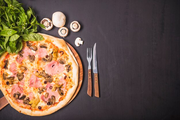 Delicious meat and mushroom pizza with fork and knife on dark background
