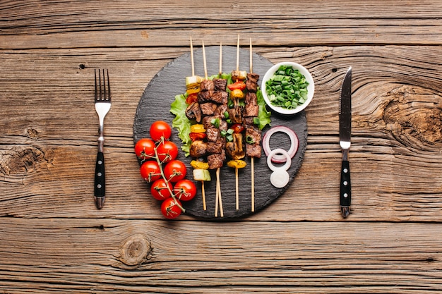 Delicious meat skewer on black slate with fork and butter knife over wooden table