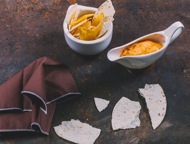 Free photo delicious mexican tortilla with nachos in bowl with cheese dip and napkin over rusty background