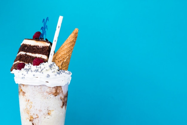 Delicious milkshake with ice cream cone and cake on blue background