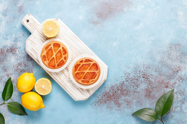 Delicious mini lemon pies with fresh lemons, top view