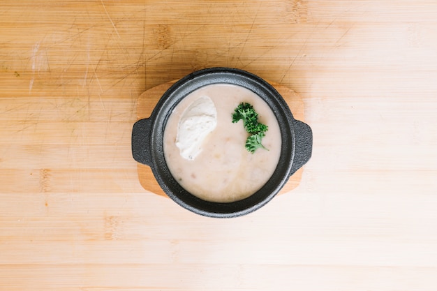 Delicious mushroom cream soup in container against wooden backdrop