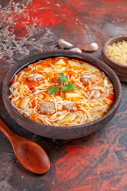 Delicious noodle soup with chicken and uncooked pasta in a small brown bowl and spoon garlic on the dark background