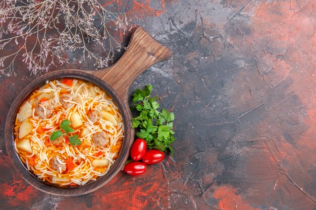 Delicious noodle soup with chicken on wooden cutting board a bunch of greens tomatoes on dark table