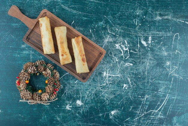 Delicious pancakes on a small tray next to a pine cone wreath on blue.