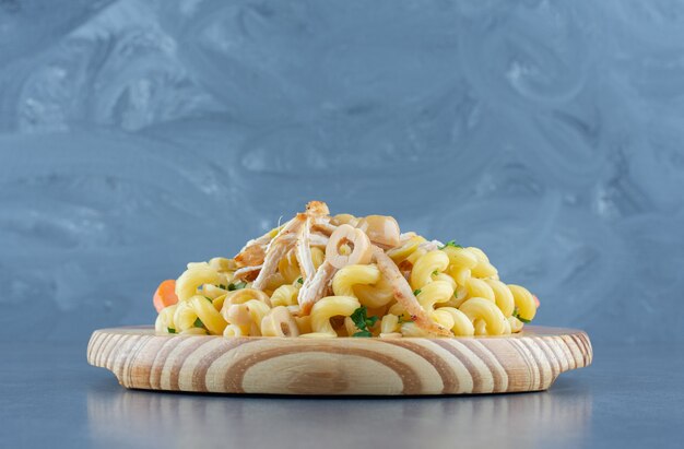 Delicious pasta with chopped chicken on wooden plate. 