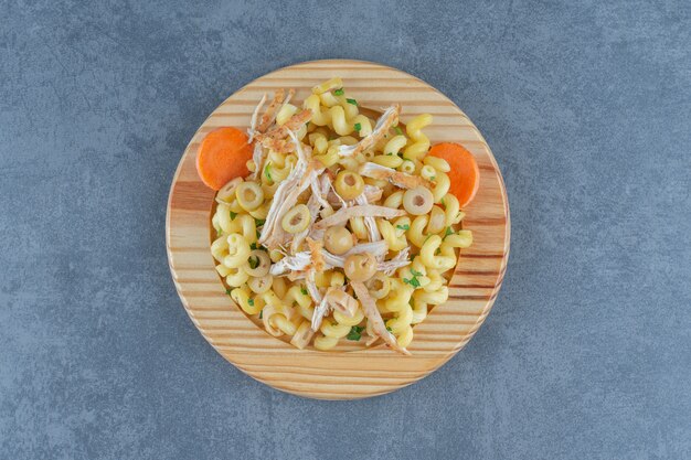 Delicious pasta with chopped chicken on wooden plate. 