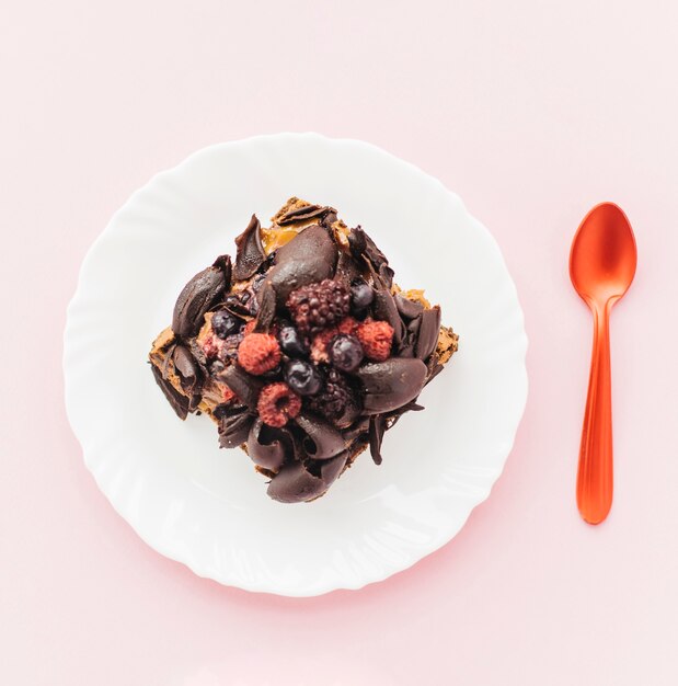 Delicious pastry on plate with spoon over pink backdrop