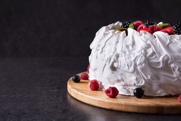 Delicious Pavlova cake with meringue topped and fresh berries on black background