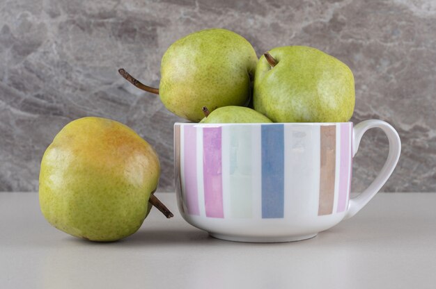 Delicious pears in and next to a large mug on marble 